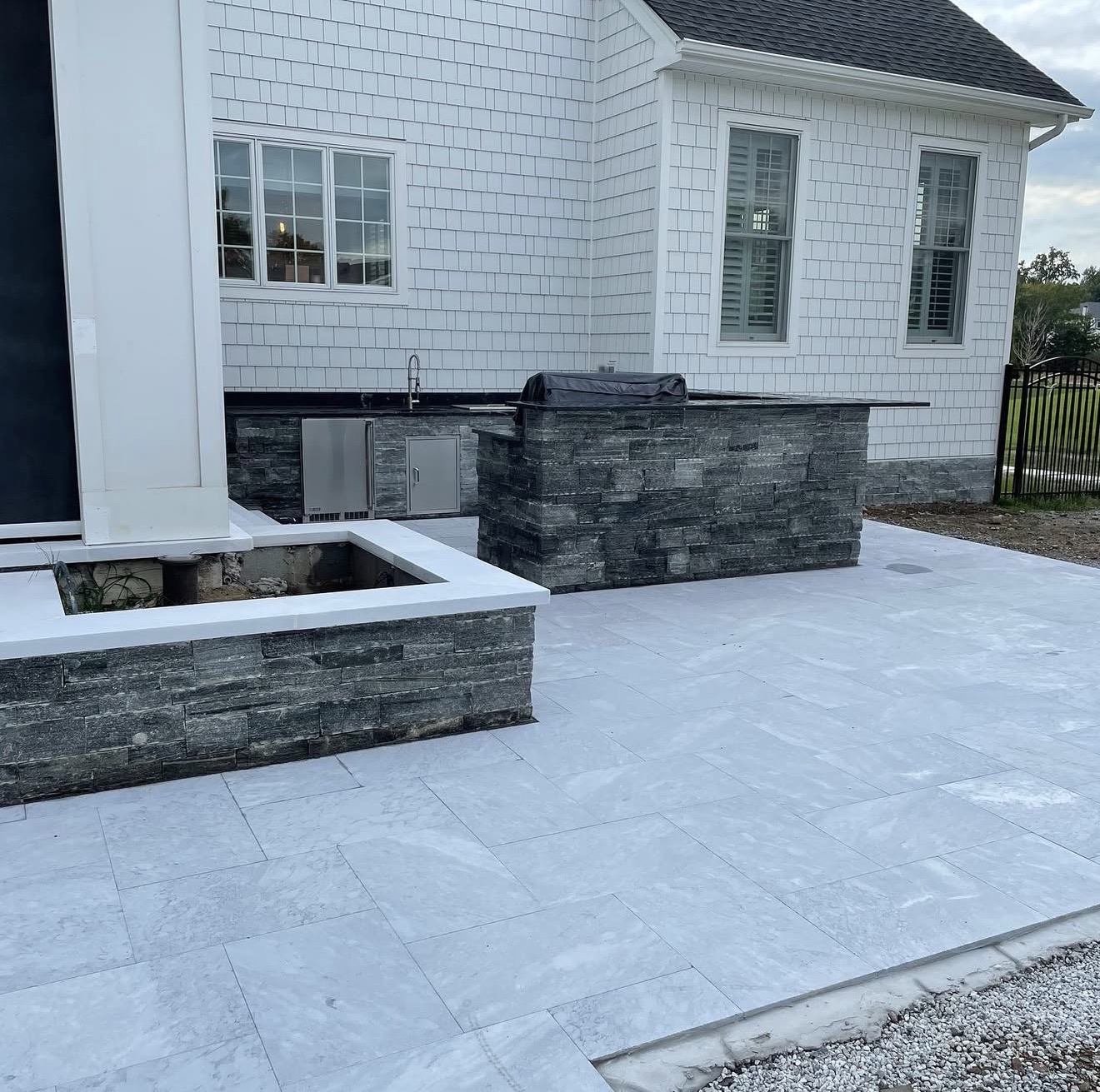 Outdoor kitchen built in stacked stone veneer with a marble paver patio and seating wall