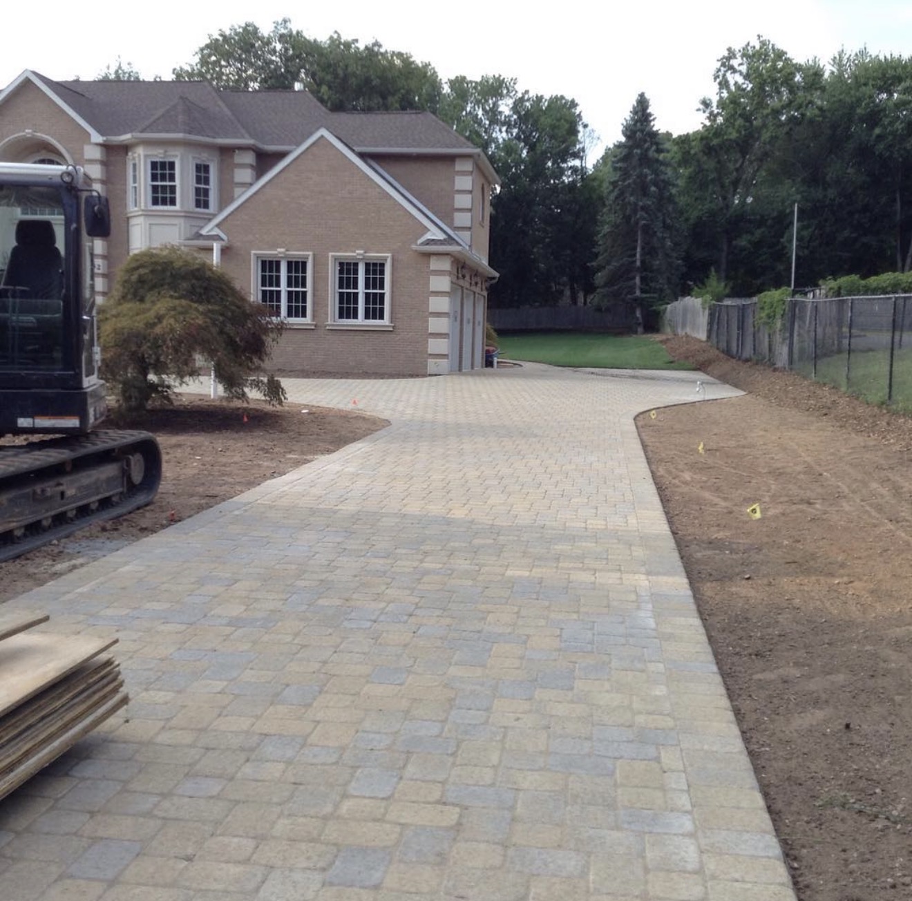 New cobblestone paver driveway with fresh grading along both sides of a New Jersey home