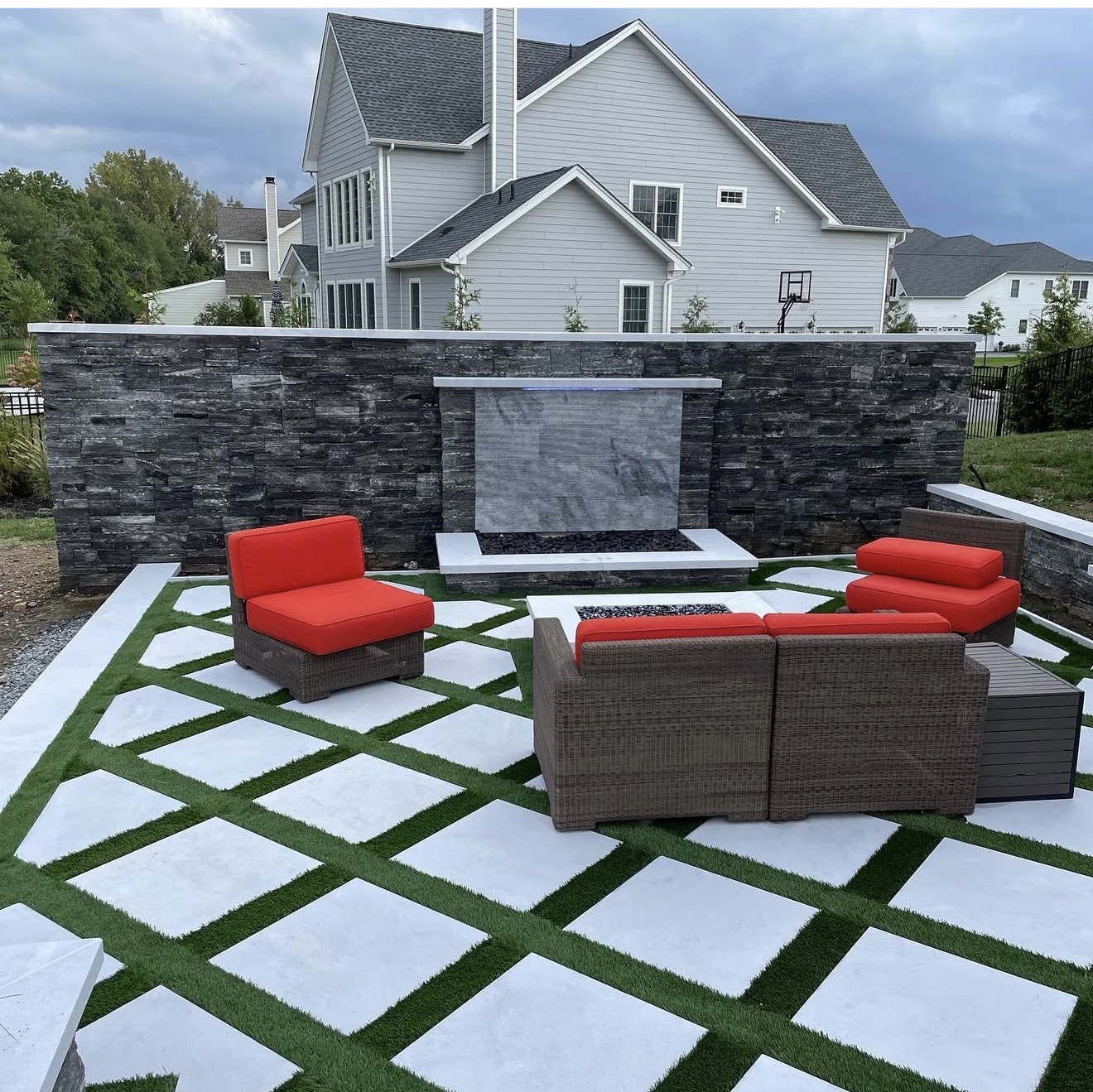 Stacked stone wall with a water feature and fire pit set in a large-format paver and turf patio