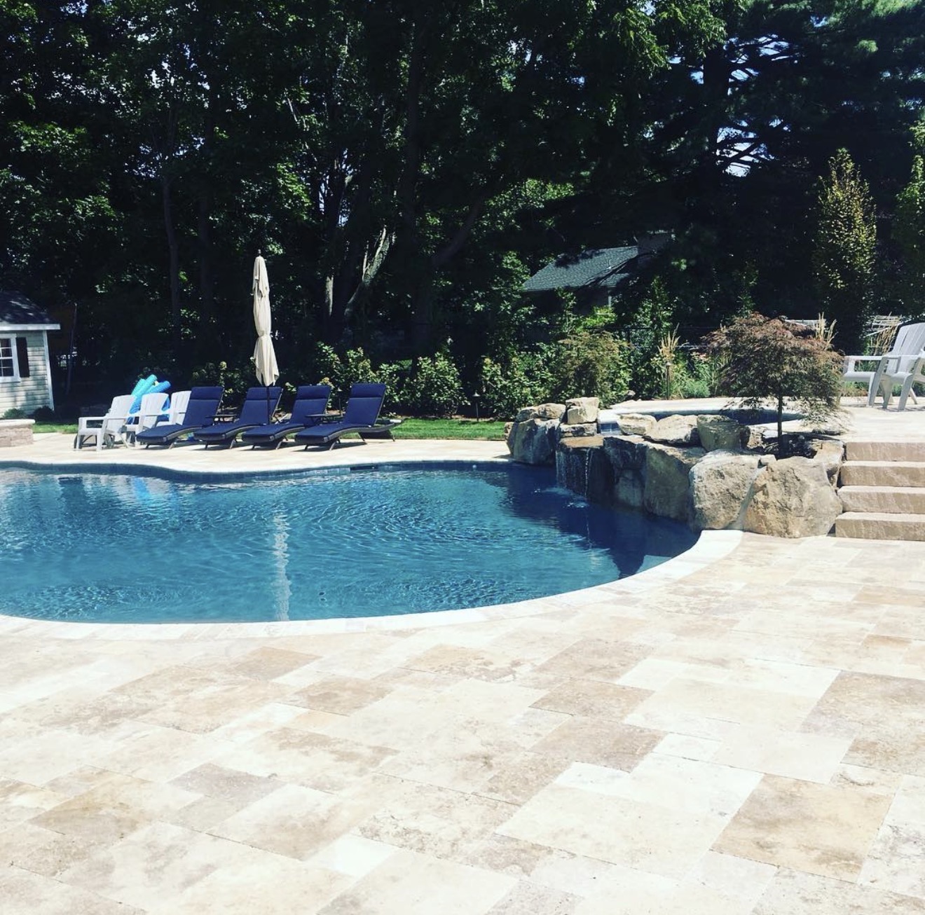 Travertine pool deck with natural boulder waterfall and stone steps at a residential pool