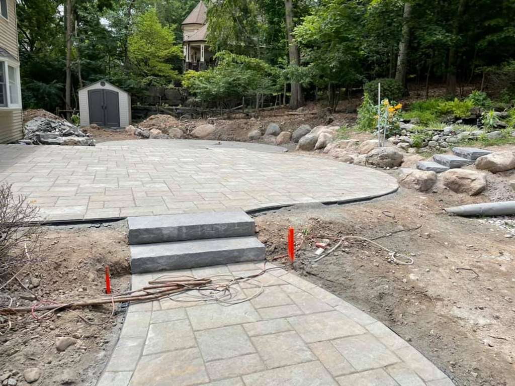 Circular paver patio with wide steps and boulder edging in a wooded backyard