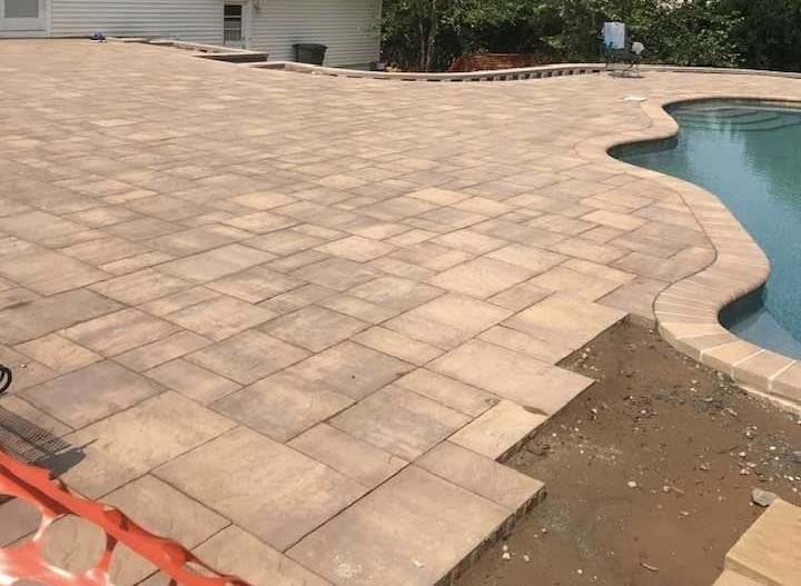 Wide paver pool deck curving around a freeform in-ground swimming pool