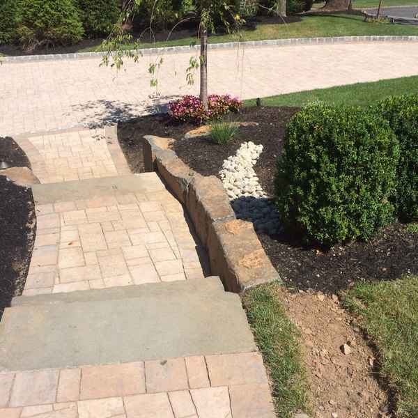 Paver walkway with bluestone steps and river rock drainage bed alongside a landscaped yard