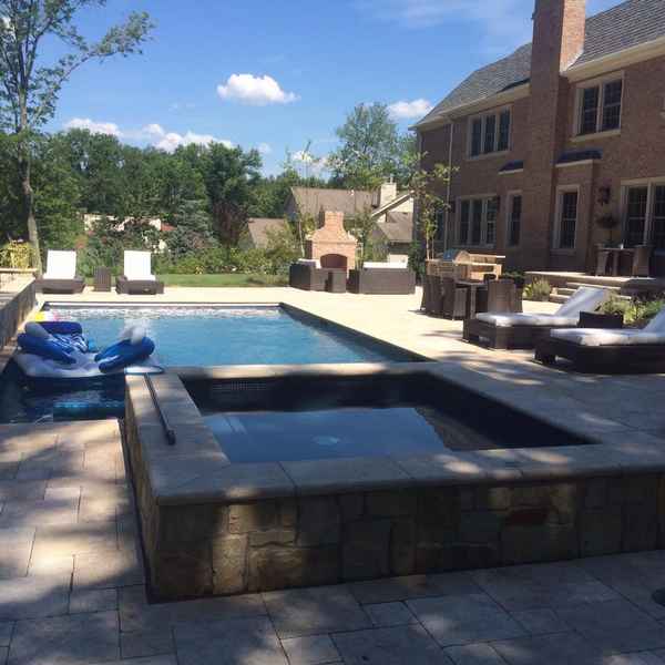 Pool and raised spa surrounded by a paver patio and outdoor living area at a brick home