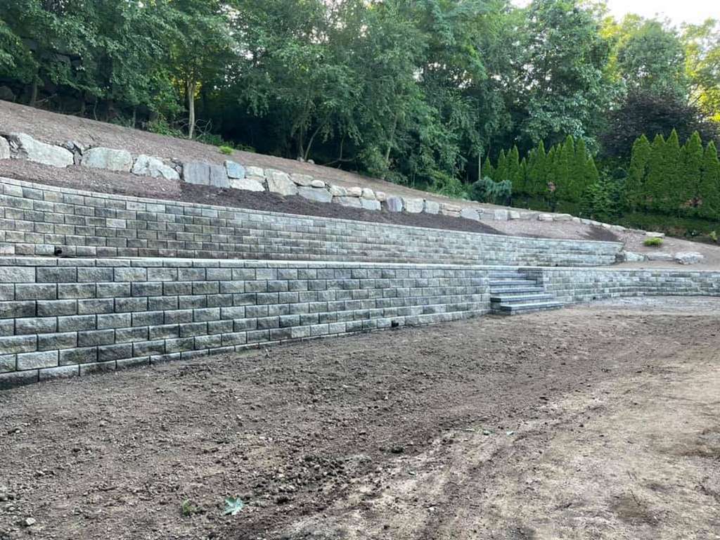 Tall tiered block retaining wall holding back a wooded slope